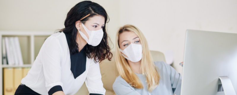 Two woment wearing a mask looking at a computer screen